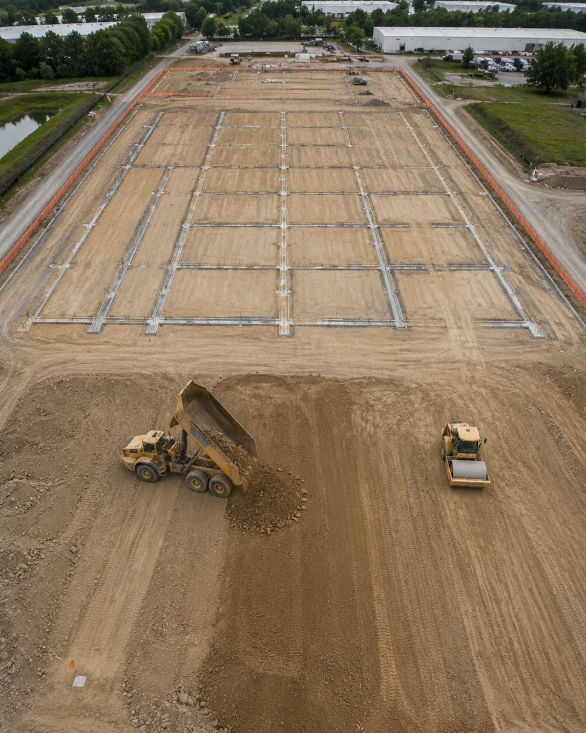 Finished graded subdivision site, silt fence lines, stabilized detention basin, golden hour